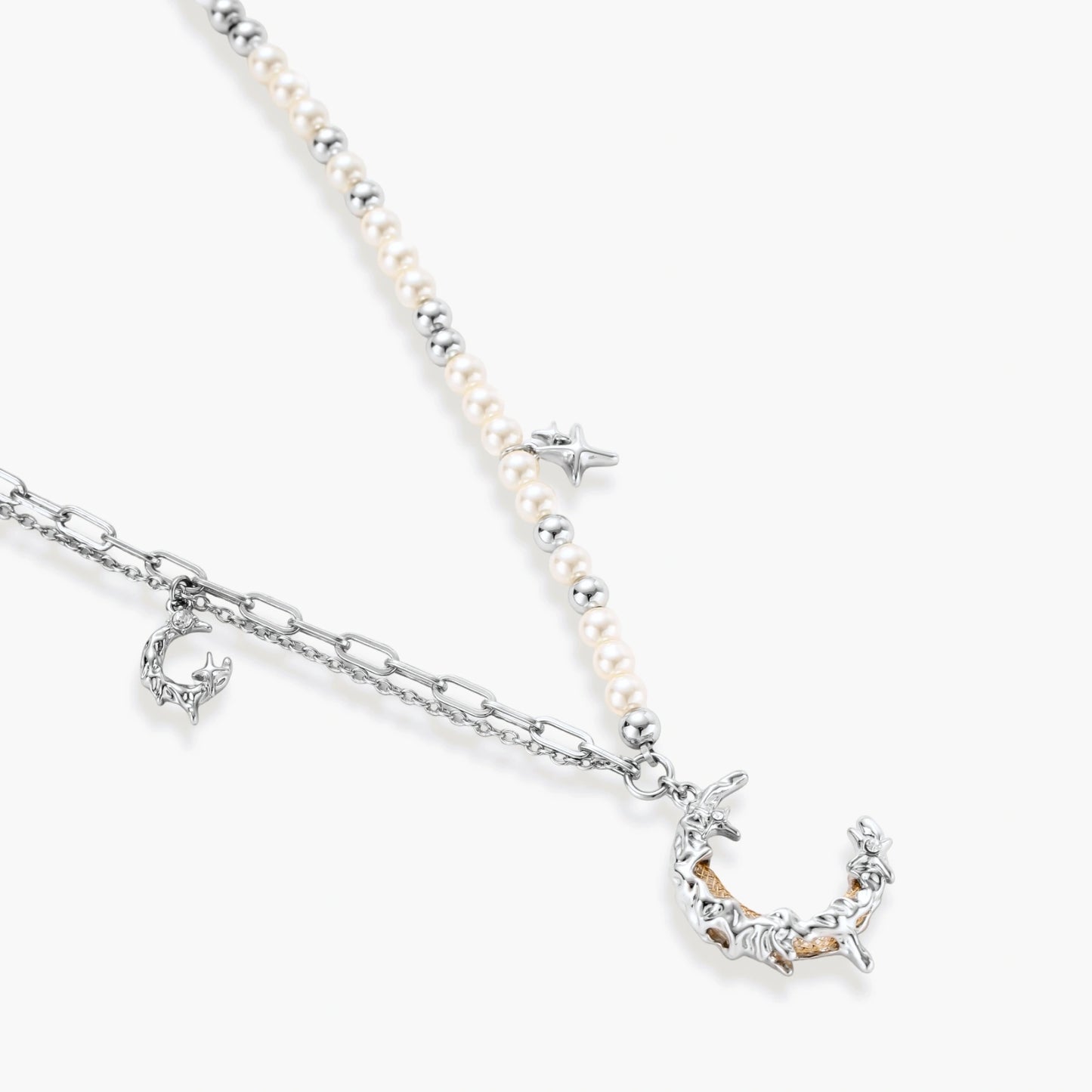 Silver-toned crescent moon pendant with star accents on pearl and chain necklace against white background.