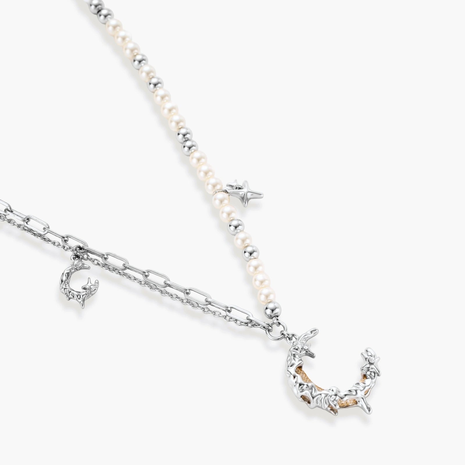 Silver-toned crescent moon pendant with star accents on pearl and chain necklace against white background.