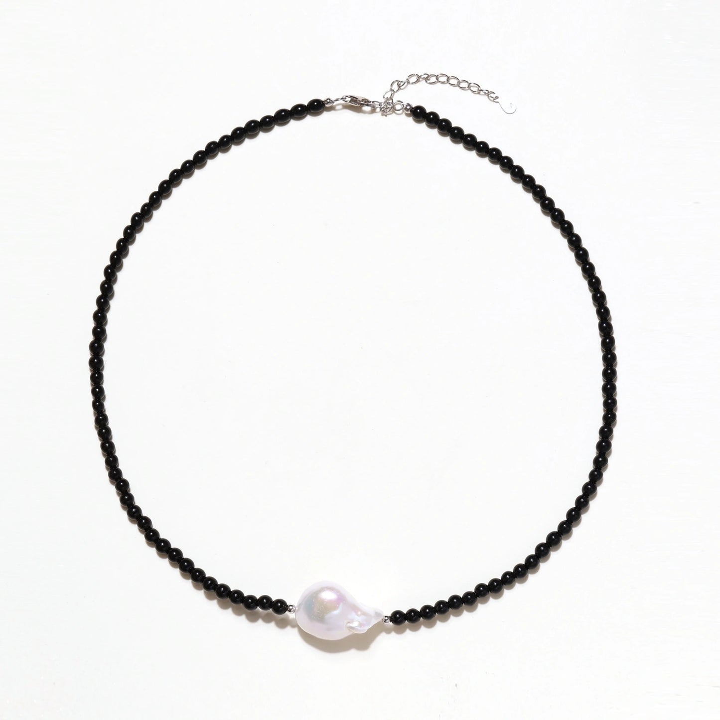 Beaded black agate necklace with iridescent baroque freshwater pearl centerpiece on cream background.