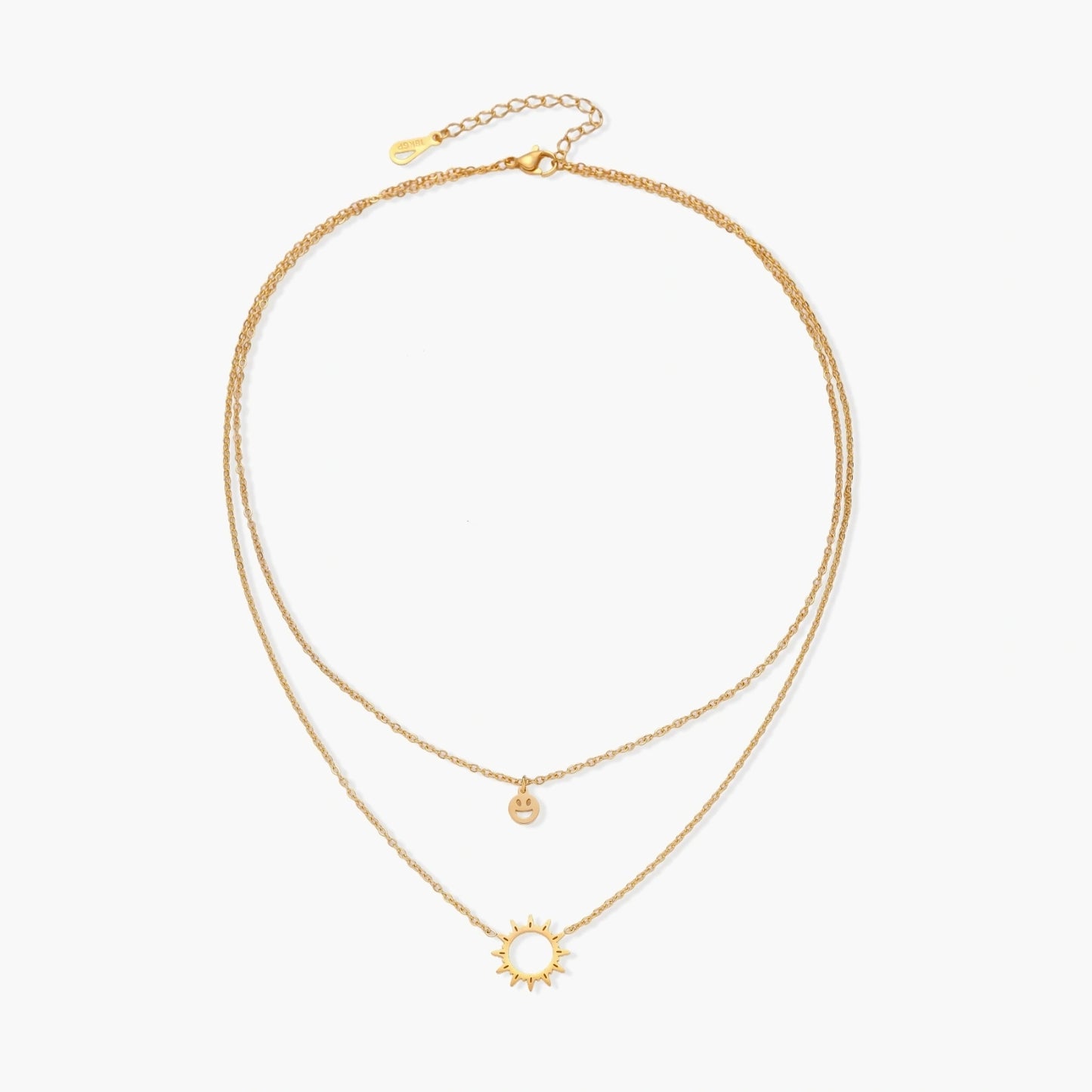 Gold layered necklace set with sunburst and smiley face pendants on delicate chains against white background.