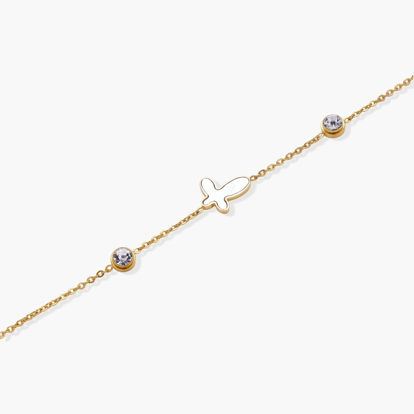 Gold chain bracelet with white mother of pearl butterfly pendant and two bezel-set crystals on cream background