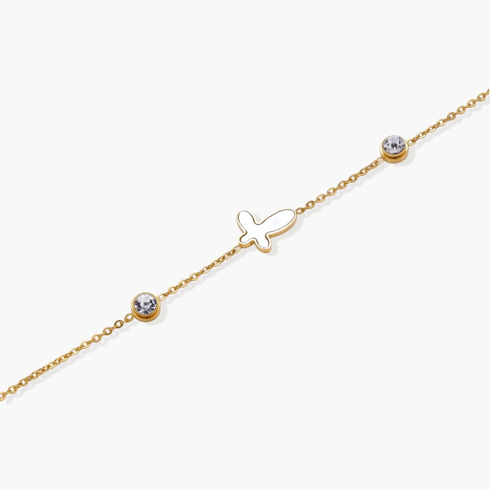 Gold chain bracelet with white mother of pearl butterfly pendant and two bezel-set crystals on cream background