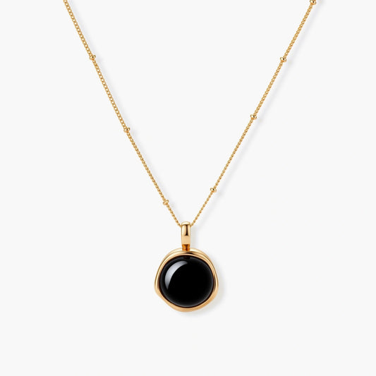 Circular black agate pendant on gold-plated sterling silver chain against cream background, showing modern minimalist design.