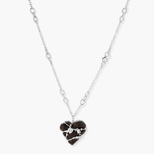 Dark ebony wood heart pendant wrapped with brass wire and zirconia crystals on adjustable chain against cream background