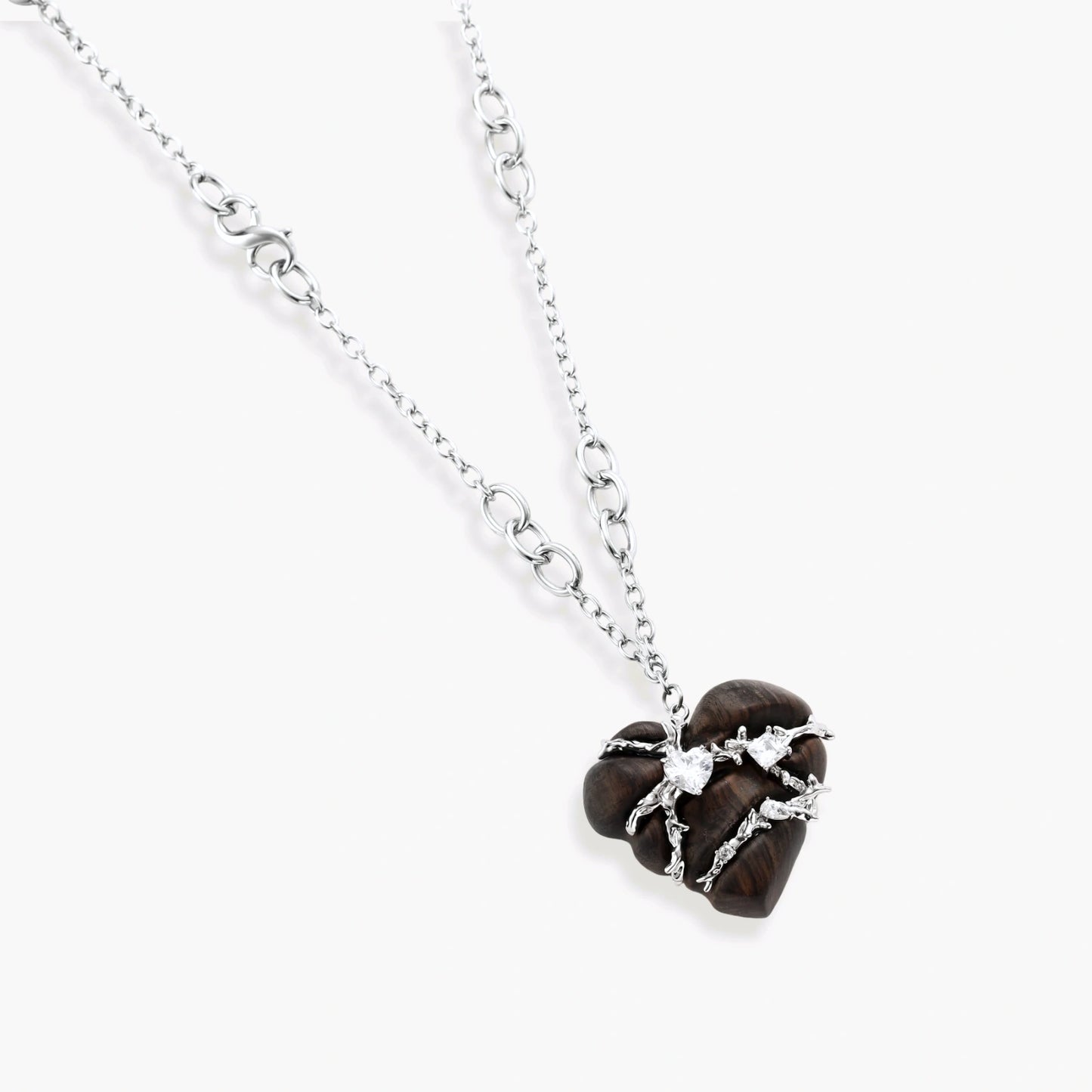 Dark ebony wood heart pendant wrapped with brass wire and zirconia crystals on adjustable chain against cream background