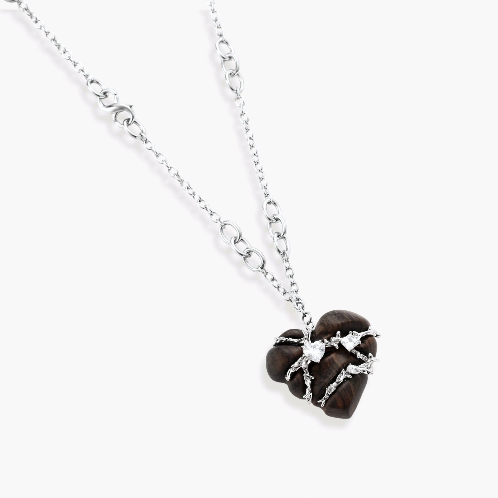 Dark ebony wood heart pendant wrapped with brass wire and zirconia crystals on adjustable chain against cream background